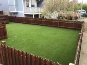Synthetic turf that was installing in a yard with a brown fence surrounding it. 